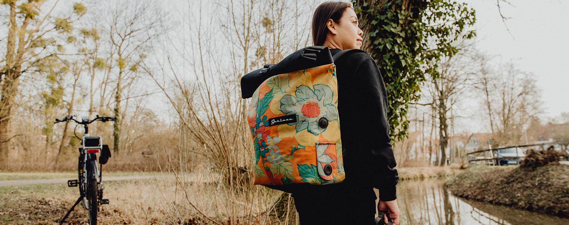 woman wearing Sarinee backpack that can be attached to the bike in the background 